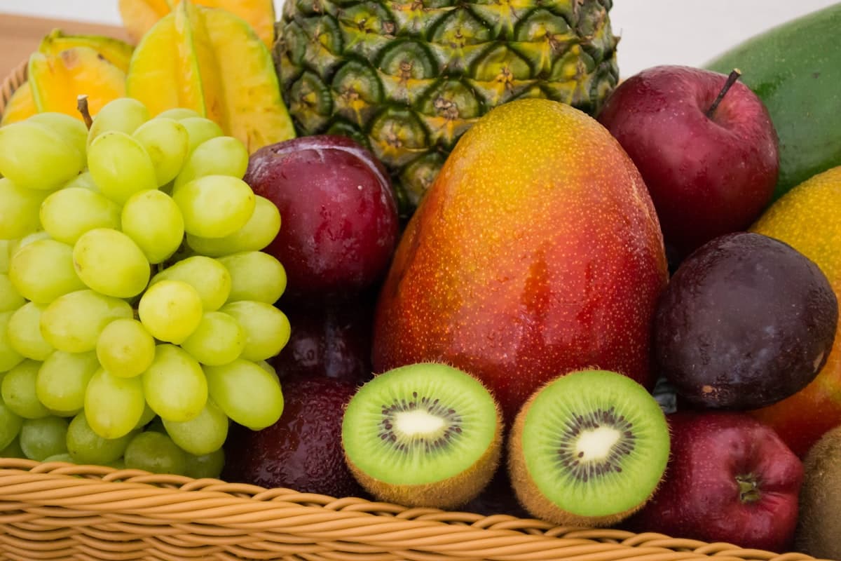 A basket of fresh grapes, mango, pineapple, kiwi and apples