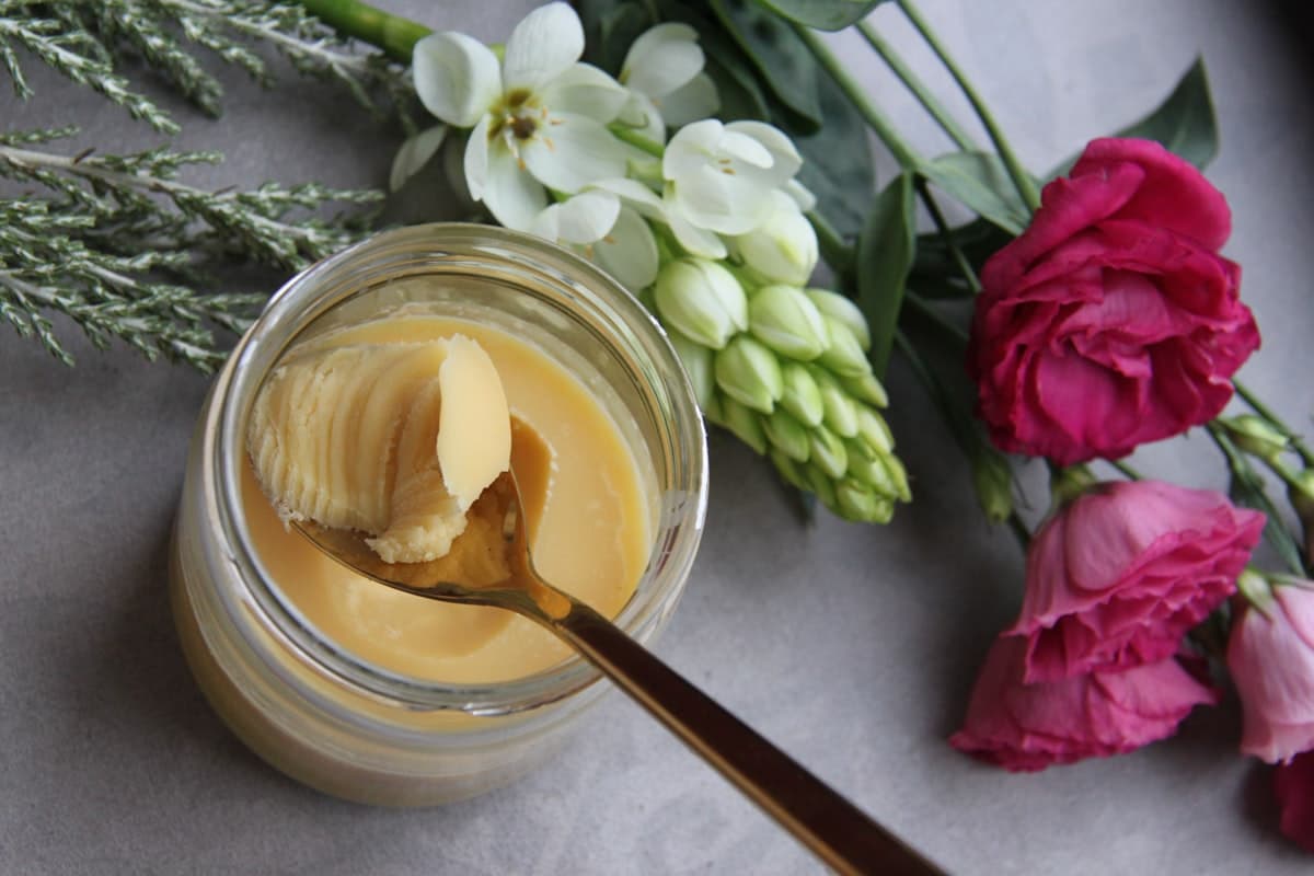 A glass jar of golden ghee with a spoon resting on top