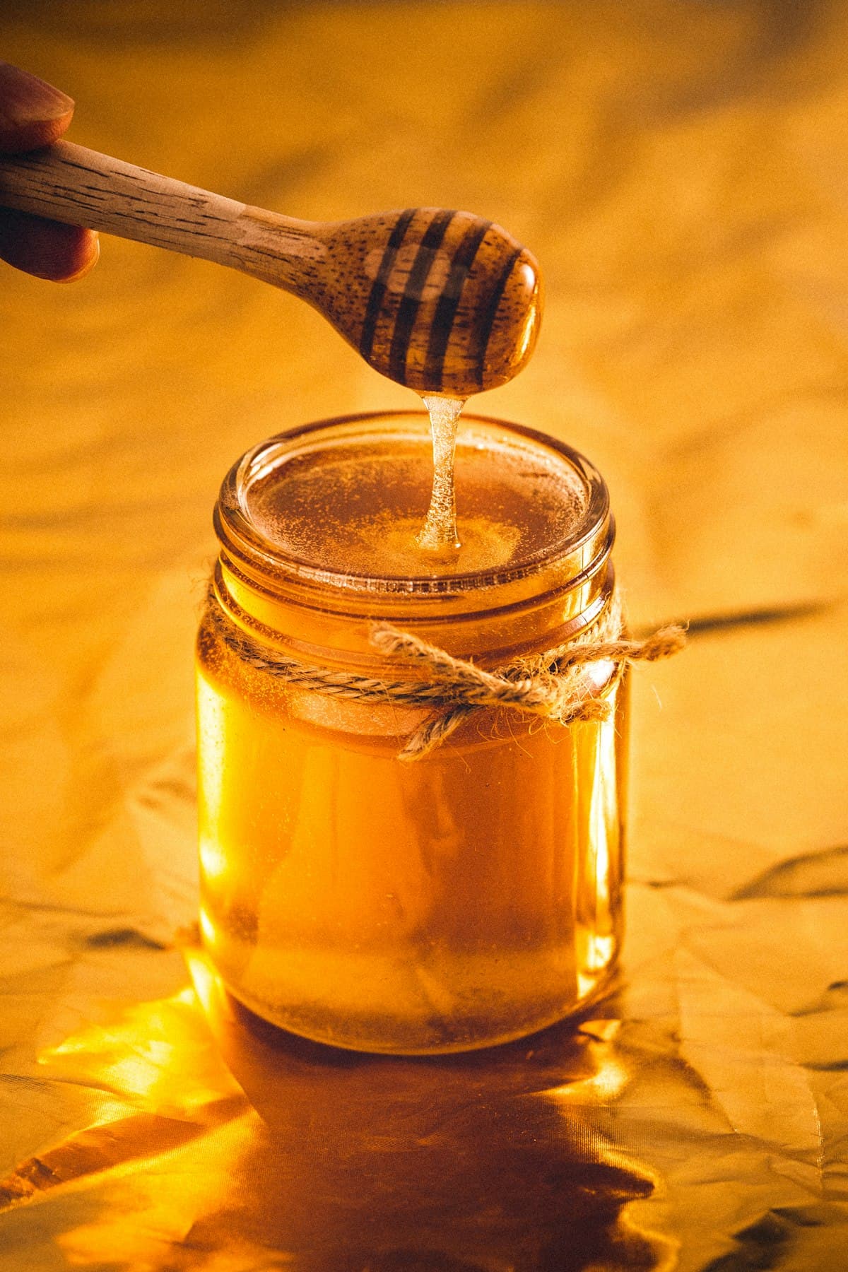 A jar of raw honey with a wooden dipper drizzling honey into it